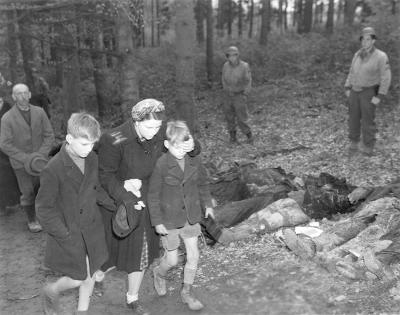 German mother shields eyes of son as she walks with other civilians past row of exhumed dead Russians outside town of Suttrop